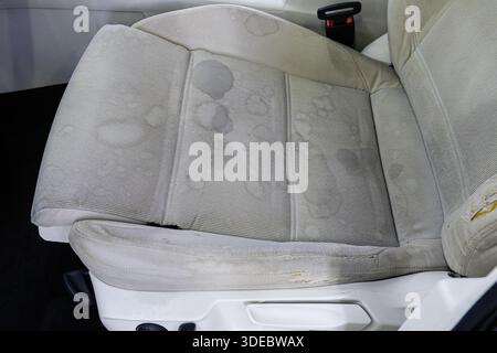 Nahaufnahme von Wasserflecken und Schmutz auf einem hellen Autositz aus Stoff. Details, die den Bedarf an Reinigung, automatischer Detaillierung und Wartung zeigen. Stockfoto