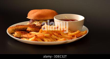 Fast Food Lunch: hamburger, Chicken Nuggets und Pommes Frites mit Ketchup auf einem runden Teller vor schwarzem Hintergrund. Nahaufnahme. Stockfoto