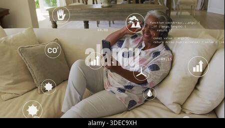 Liegende ältere Frau mit Smartphone und Blick auf AR-Symbole auf hellem Sofa und gemusterter Bluse Stockfoto