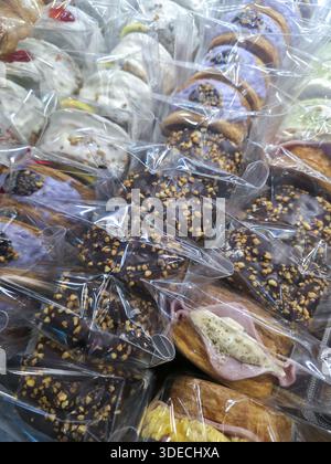 Auswahl an frischem süßem Gebäck, verpackt in durchsichtigen Plastiktüten, mit verführerischem Schokoladen-glasiertem Donut mit Nüssen und cremig gefülltem Brötchen Stockfoto