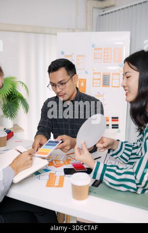 Eine Gruppe von UX/UI-Designern arbeitet gemeinsam kreative Ideen aus und diskutiert Farbpaletten und Layoutkonzepte für eine neue mobile Anwendungsoberfläche Stockfoto
