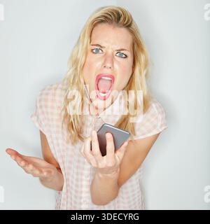 Wütende Frau, Porträt und Schreien mit Lautsprechertelefon im Studio für Kampf auf weißem Hintergrund. Weibliche Person, Model oder Schreie mit Handy Stockfoto