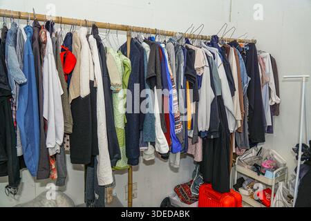 Überfüllte Garderobe mit Kleidung, die auf einem Bambusständer hängt, roter Koffer und Ablagefach in einem Wohnbereich. Stockfoto