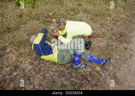 Naturfotografen in Camouflage- und Neonjacken, die Fotos auf einem Smartphone ansehen, während sie draußen auf dem Boden liegen. Stockfoto
