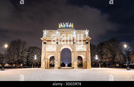 Der Arc de Triomphe du Carrousel befindet sich in der Nähe des Louvre in Paris, Frankreich. Die nächtliche Winterszene zeigt das beleuchtete Denkmal und das schneebedeckte Gelände mit einem Riesenrad in der Ferne Stockfoto