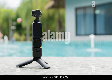 Action kleine Kamera und Stativ auf dem Boden in der Nähe eines Schwimmbadhintergrunds mit Kopierraum. Action-Kamera für Foto und Video. Stockfoto