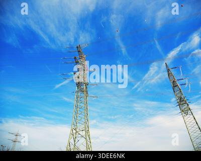 Elektrische Sendetürme und Stromleitungen von unten vor dem dramatischen blauen Himmel mit Wolken Stockfoto
