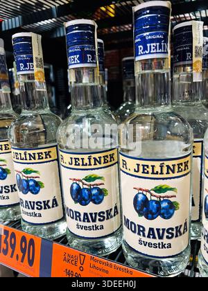 Brünn, Tschechische Republik - 29. November 2025: Glasflaschen mit Moravská švestka Pflaumenschnaps auf einem Ladenregal mit blauen Etiketten und orangefarbenen Preisschildern. Stockfoto