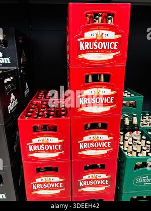 Brünn, Tschechische Republik - 29. November 2025: In knallroten Kisten werden Bierflaschen in einem Ladenregal aufbewahrt, was eine kühne Präsentation von Krušovice Lager schafft. Stockfoto