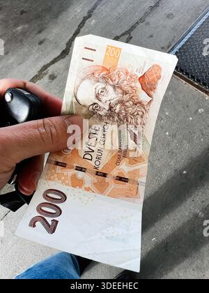 Brünn, Tschechische Republik - 29. November 2025: Nahaufnahme einer Hand, die eine 200-Kronen-Banknote neben Autoschlüsseln auf einem Bürgersteig hält. Stockfoto