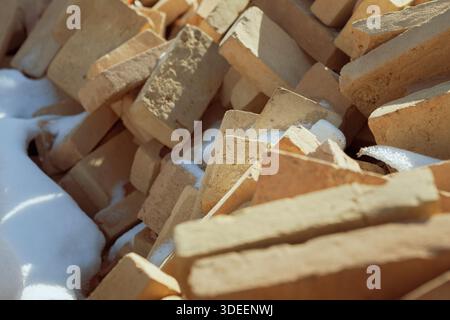 Hochwinkel, Nahaufnahme von Sandziegeln, die sich unregelmäßig auftürmen und mit frischem weißem Schnee bedeckt sind. Texturen aus rauen Ziegeln und kristallinem Schneekontrast Stockfoto