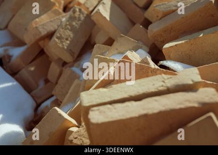Hochwinkel, Nahaufnahme von Sandziegeln, die sich unregelmäßig auftürmen und mit frischem weißem Schnee bedeckt sind. Texturen aus rauen Ziegeln und kristallinem Schneekontrast Stockfoto