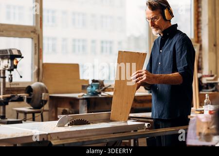 Zimmermann mit Noise Cancelling-Kopfhörern und Holzplanke || Modell veröffentlicht Stockfoto
