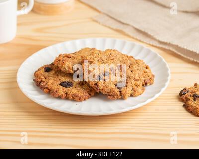 Frisch gebackene Haferflocken mit Rosinenkeksen auf einem weißen geriffelten Teller auf einem Holztisch. Kaugummi, süße Leckereien aus Hafer, Rosinen und klassischem Backofen Stockfoto