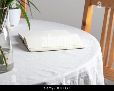 Öffnen Sie das schwarze Notizbuch auf einer weißen Tischdecke. Leere cremefarbene Seiten mit genähter Bindung liegen flach und eignen sich ideal zum Schreiben, Skizzieren oder für kreative Arbeiten Stockfoto