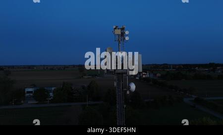 Mobilfunkturm steht vor dem dunkelblauen Himmel, ausgestattet mit verschiedenen Antennen für drahtlose Kommunikation und Mobilfunkdienste im gesamten Po Val Stockfoto