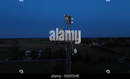 Mobilfunkturm steht vor dem dunkelblauen Himmel, ausgestattet mit verschiedenen Antennen für drahtlose Kommunikation und Mobilfunkdienste im gesamten Po Val Stockfoto