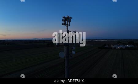 Mobilfunkturm steht vor dem dunkelblauen Himmel, ausgestattet mit verschiedenen Antennen für drahtlose Kommunikation und Mobilfunkdienste im gesamten Po Val Stockfoto