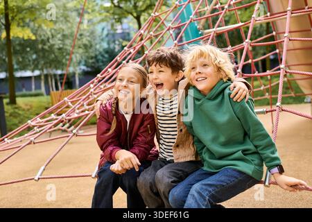Drei fröhliche Kinder lachen im Herbst gemeinsam auf einer einzigartigen Kletterstruktur. Stockfoto