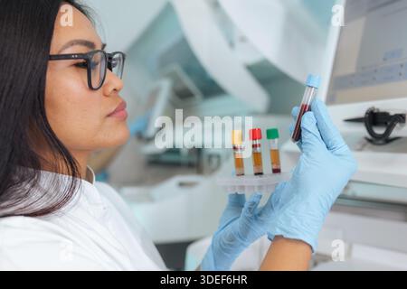 Eine professionelle asiatische Wissenschaftlerin untersucht Blutproben in einem gut ausgestatteten pharmazeutischen Labor und führt dabei klinische Tests durch. Stockfoto