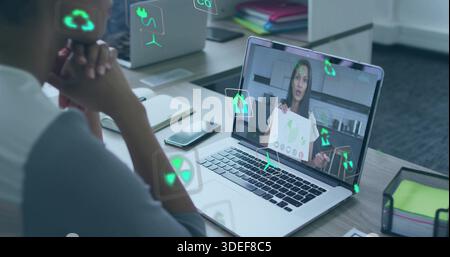Zeigt einen geöffneten Laptop mit einem Remote-Referenten, der ein grünes Blatt am Bürotisch hält, mit AR-Symbolen Stockfoto