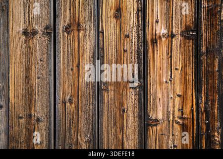 Nahaufnahme alter vertikaler Holzdielen mit sichtbarer Körnung, Knoten und Nagelspuren. Natürliche Alterung und warme Brauntöne sorgen für eine starke rustikale Textur. Stockfoto
