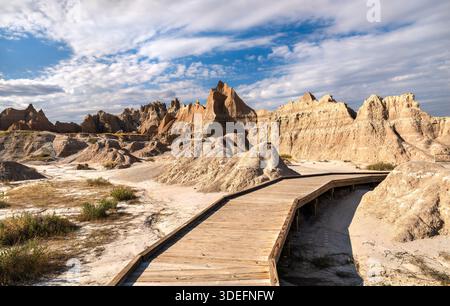 Fossil Exhibit Trail im Badlands National Park, South Dakota, USA. Hölzerne Promenade schlängelt sich durch trockene Landschaft und zerklüftete Felsformationen unter einem bl Stockfoto