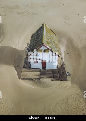 Aus der Vogelperspektive eines verwitterten Strandhauses, das einsam inmitten der riesigen Weite des goldenen Sandes steht, ein Beweis für Widerstandsfähigkeit gegen die Elemente, Cost Stockfoto
