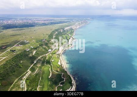 Blick aus der Vogelperspektive auf das Thracian Cliffs Golf & Beach Resort, wo die lebhaften grünen Fairways auf das türkisfarbene Wasser des Schwarzen Meeres in Bozhurets, Bulgarien, treffen. Stockfoto