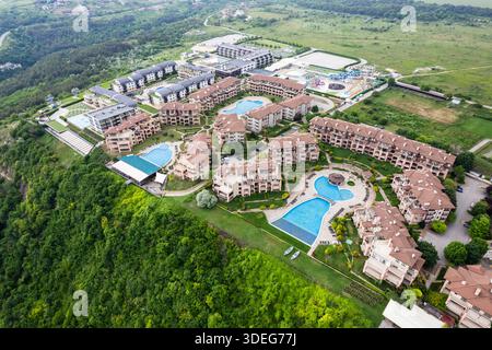 Blick aus der Vogelperspektive auf luxuriöse Resortgebäude mit mehreren Pools, die sich über eine Klippe stürzen, eingebettet zwischen üppigem Grün und dem fernen Meer, Thracian CLI Stockfoto