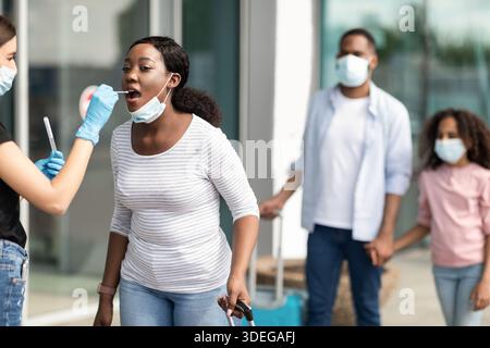 Medizinischer Arbeiter, der COVID-19 PCR-Test für schwarzen weiblichen Touristen macht Stockfoto