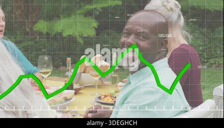 Lächelnder Seniorenmann in Minzhemd am Gartentisch mit Wein und grünem Graphen Stockfoto