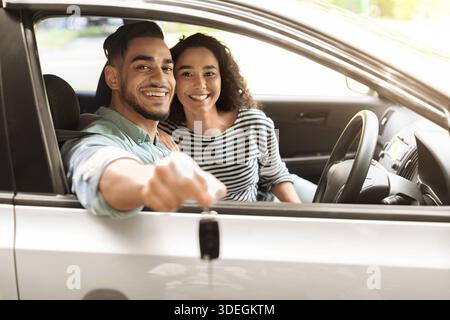 Glückliches junges Paar aus dem Nahen Osten, das den Schlüssel aus dem Auto zeigt Stockfoto