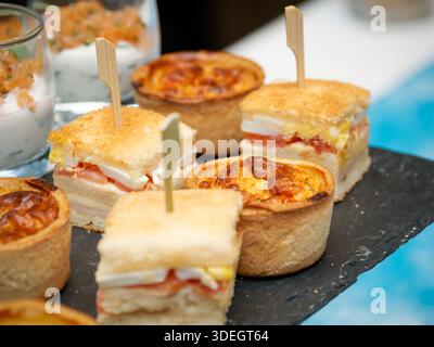 Auswahl an Gourmet-Fingerfood einschließlich Mini-Quiches, mehrschichtigen Sandwiches und Garnelen-Verrines, die am Catering-Buffet serviert werden. Stockfoto