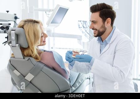 Fröhlicher Mann Arzt Zahnarzt zeigt Kiefer Miniatur zum Patienten Stockfoto