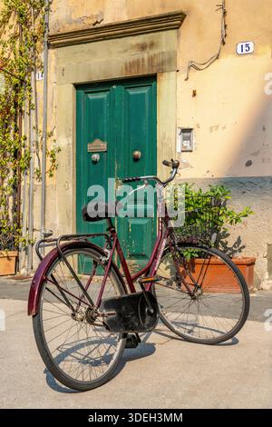 Ein geparktes altmodisches Fahrrad mit Korb, vor einer Tür an der Piazza Cittadella, Lucca, Italien. Stockfoto