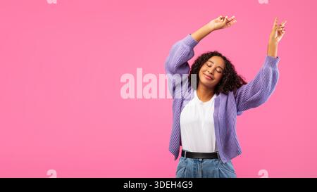 Frau tanzt glücklich vor rosafarbenem Hintergrund mit erhobenen Armen in der Feier Stockfoto