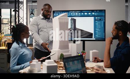 Stadtentwicklung Diversität Team diskutiert Immobilieninvestitionen neue Strategie für die Projektgenehmigung in einem hellen Büroumfeld, analysiert Blaupausen und 3D-Modelle auf Architektursoftware. Stockfoto