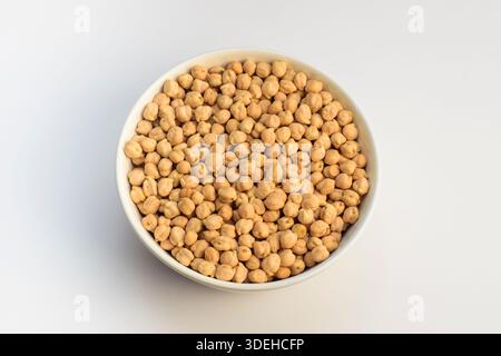 Blick von oben auf eine weiße Schüssel gefüllt mit ungekochten getrockneten Kichererbsen auf hellem Hintergrund. Saubere, einfache Zusammensetzung. Stockfoto