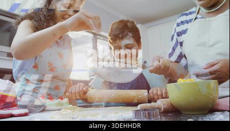 Oma mit Sieb durchsickern, während Mama den Jungen mit Teig an der Küchentheke in Schürzen führt Stockfoto