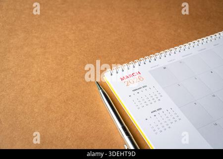 März 2026 Kalender auf brauner Oberfläche mit einem Stift daneben. Draufsicht, Kopierraum. Stockfoto