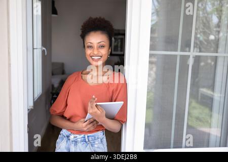 Fröhliche junge afroamerikanische Maklerin, die vor der Tür steht Stockfoto