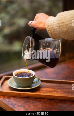Eine Frau, die frisch gebrühten Kaffee in einer farbigen Tasse in einem Café serviert. Stockfoto