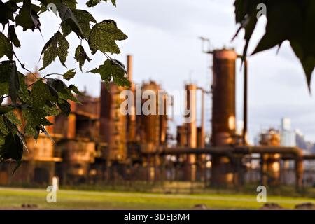 Verrostete Industriestrukturen an einem ehemaligen Gaswerk in Seattle, Washington, mit hochaufragenden Rohren und altem Metall vor einer urbanen Landschaft. Stockfoto