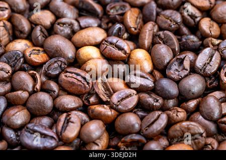 Nahaufnahme gemischte Kaffeebohnen mit verschiedenen Farbtönen und kühlender Tablettenatmosphäre, die kleine Rösterei und industrielle Wärme vermitteln Stockfoto