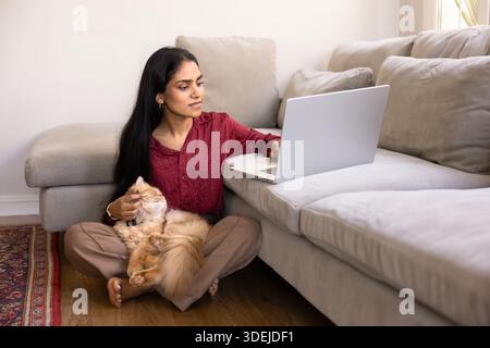 Positive junge Indianerin, die flauschige rote Katze in den Armen hält Stockfoto