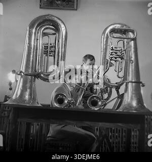 Slawjansk, Region Donezk, ukrainische SSR, Sowjetunion, 1980er Jahre Eine Probe einer Blaskapelle in einem Kulturzentrum oder Club. Zwei Musiker üben: Der eine spielt eine große Tuba, der andere spielt an einem Tisch ein Tenorhorn (Alt). Zwei massive Tubas ruhen auf dem Tisch im Vordergrund, die die Szene visuell umrahmen. Das Zimmer ist mit einfachen Möbeln, einer Lampe und einem Gemälde an der Wand ausgestattet. Dieses Archivfoto zeigt das Engagement von Amateurmusikern und die Atmosphäre der musikalischen Bildung im friedlichen Donbass. Stockfoto