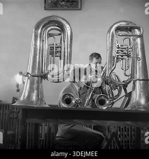 Slawjansk, Region Donezk, ukrainische SSR, Sowjetunion, 1980er Jahre Eine Probe einer Blaskapelle in einem Kulturzentrum oder Club. Zwei Musiker üben: Der eine spielt eine große Tuba, der andere spielt an einem Tisch ein Tenorhorn (Alt). Zwei massive Tubas ruhen auf dem Tisch im Vordergrund, die die Szene visuell umrahmen. Das Zimmer ist mit einfachen Möbeln, einer Lampe und einem Gemälde an der Wand ausgestattet. Dieses Archivfoto zeigt das Engagement von Amateurmusikern und die Atmosphäre der musikalischen Bildung im friedlichen Donbass. Stockfoto