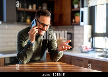 Selbstbewusster, lächelnder Geschäftsmann mit Smartphone im Heimbüro. Überprüfen neuer E-Mails, Videoanrufe Stockfoto