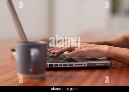 Tippen Auf Laptop Am Schreibtisch Zu Hause Mit Becher – Konzentriertes Arbeiten Am Gemütlichen Arbeitsbereich Stockfoto